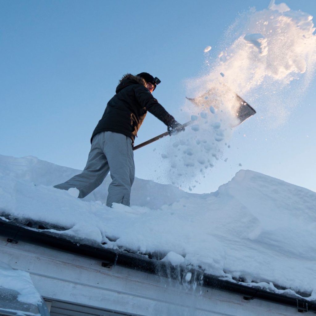 man shoveling snow off roof of house