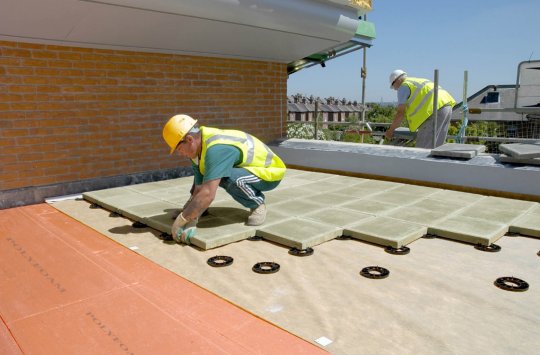 Two men in yellow vests working on a roof